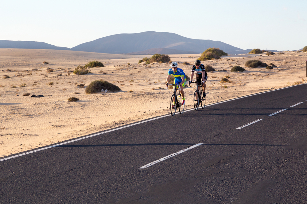 Fuerteventura, Canary Islands, Spain - 12/21/2017. Cyclists on a road in a Corralejo Natural Park. Bicycling biking tour travel trip. Two guys riding a bike in a desert highway