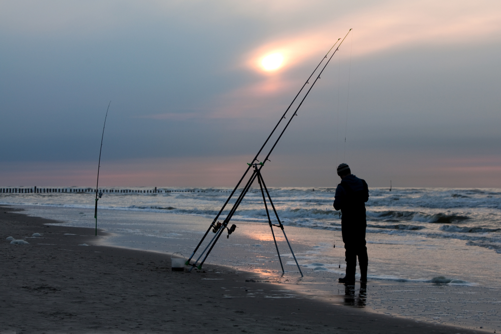 silhouette of a man with big fishing rods on the beach of the north sea island wangerooge, germany in front of dramatic sky while sunset