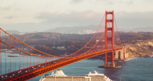 Beautiful panorama view of cruise ship passing famous Golden Gate Bridge with the skyline of San Francisco in the background in beautiful golden evening light at sunset in summer, California, USA