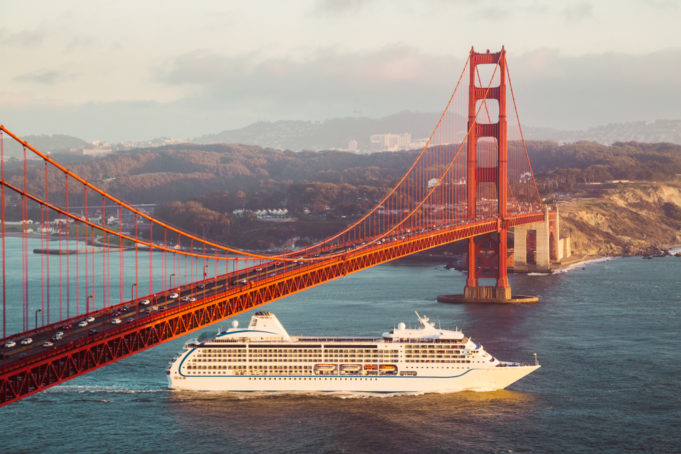 Beautiful panorama view of cruise ship passing famous Golden Gate Bridge with the skyline of San Francisco in the background in beautiful golden evening light at sunset in summer, California, USA