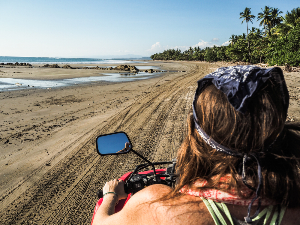 young woman from the back driving quad on the beach in costa rica
