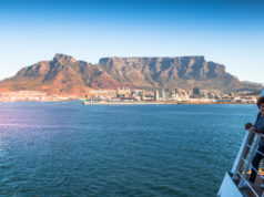 Cape Town, South Africa - April 24, 2017: Unidentified passengers on board a cruise ship watch from deck as the liner leaves Table Bay Harbor with Table Mountain forming a backdrop
