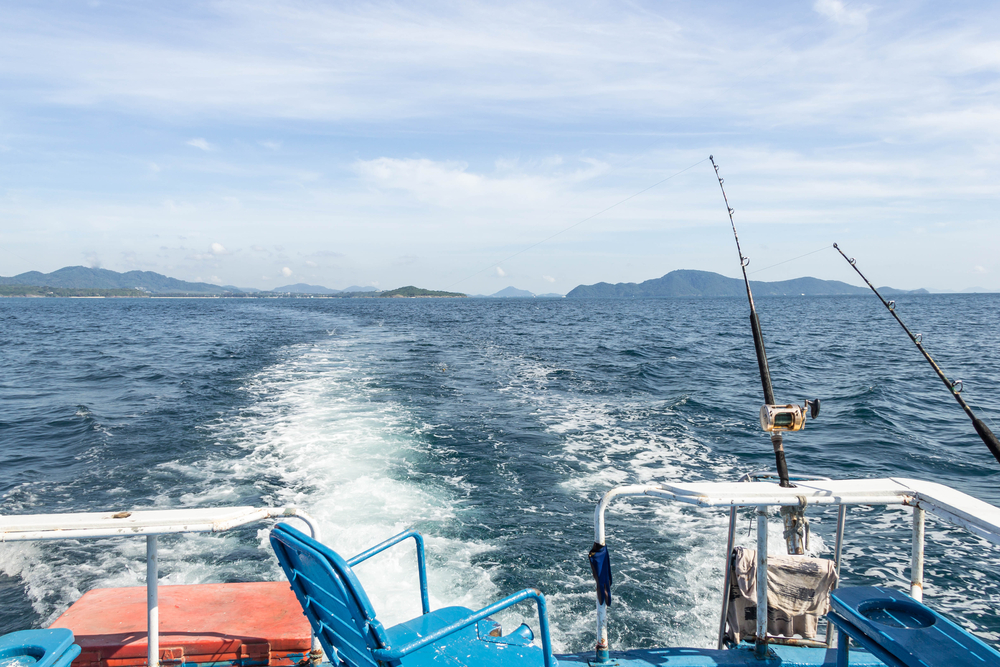 Trolling fishing boat rod and golden saltwater reels deep blue ocean sea wake