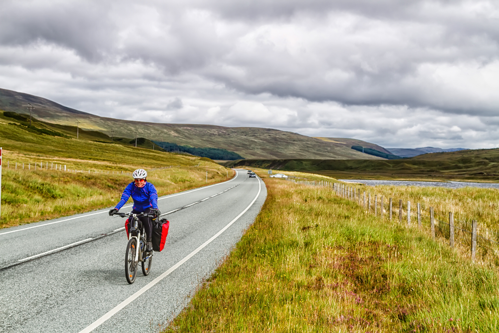 HIGHLANDS, SCOTLAND - AUGUST 15, 2016: Solo female cyclist cycle through Scottish mountains with her bicycle fully loaded with equipment and camping gear.