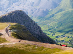A train descends from the summit of Snowdon Mountain on the narrow gauge rack mountain railway with the Llanberis valley and spoil heaps of Dinorwig slate quarry in the distance.