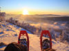 Winter sport activity concept. Hiker looking over his snowshoes at the beautiful landscape in the French mountains during sunset.